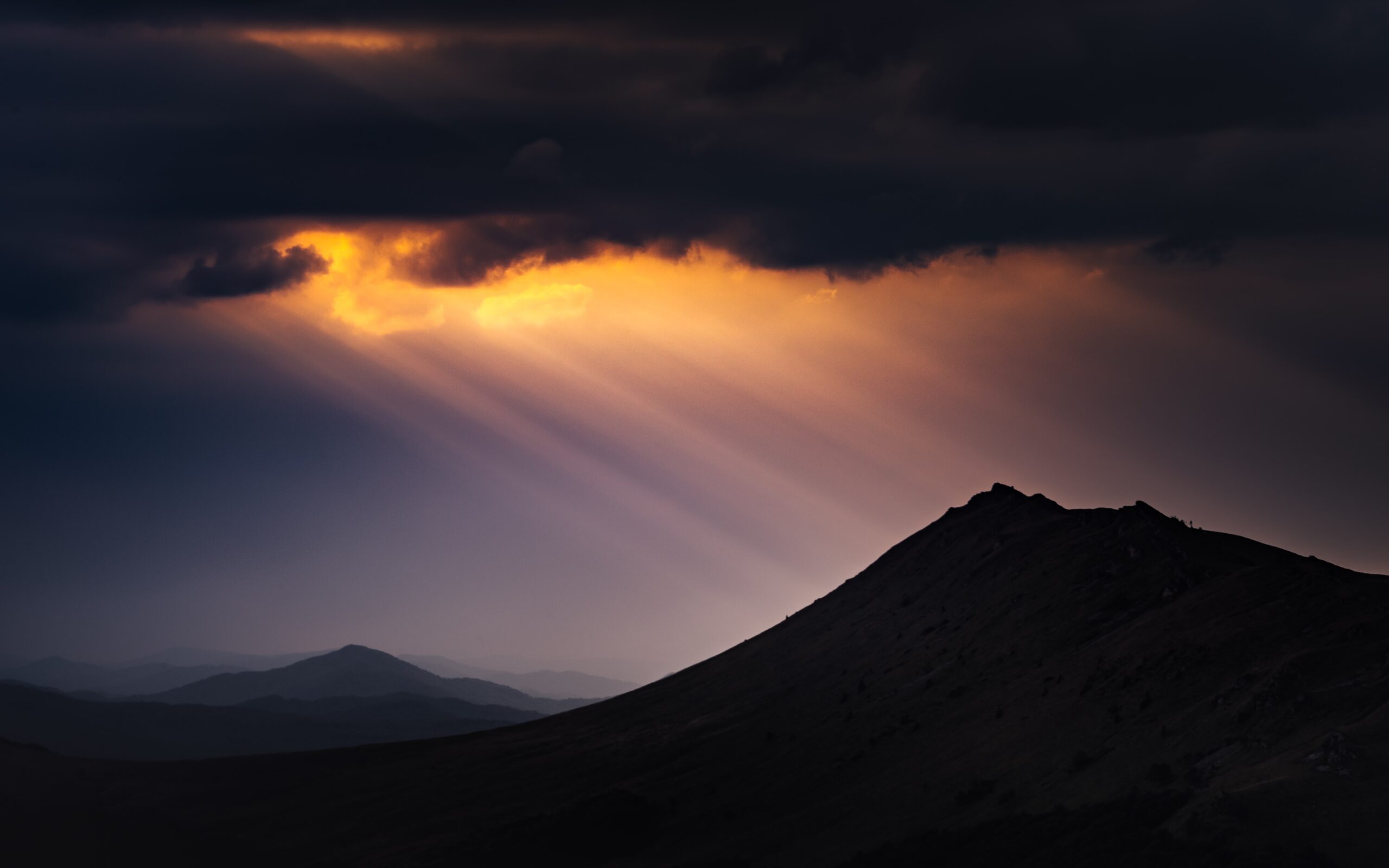 Brilliant golden rays of light through dark clouds descend upon a mountain