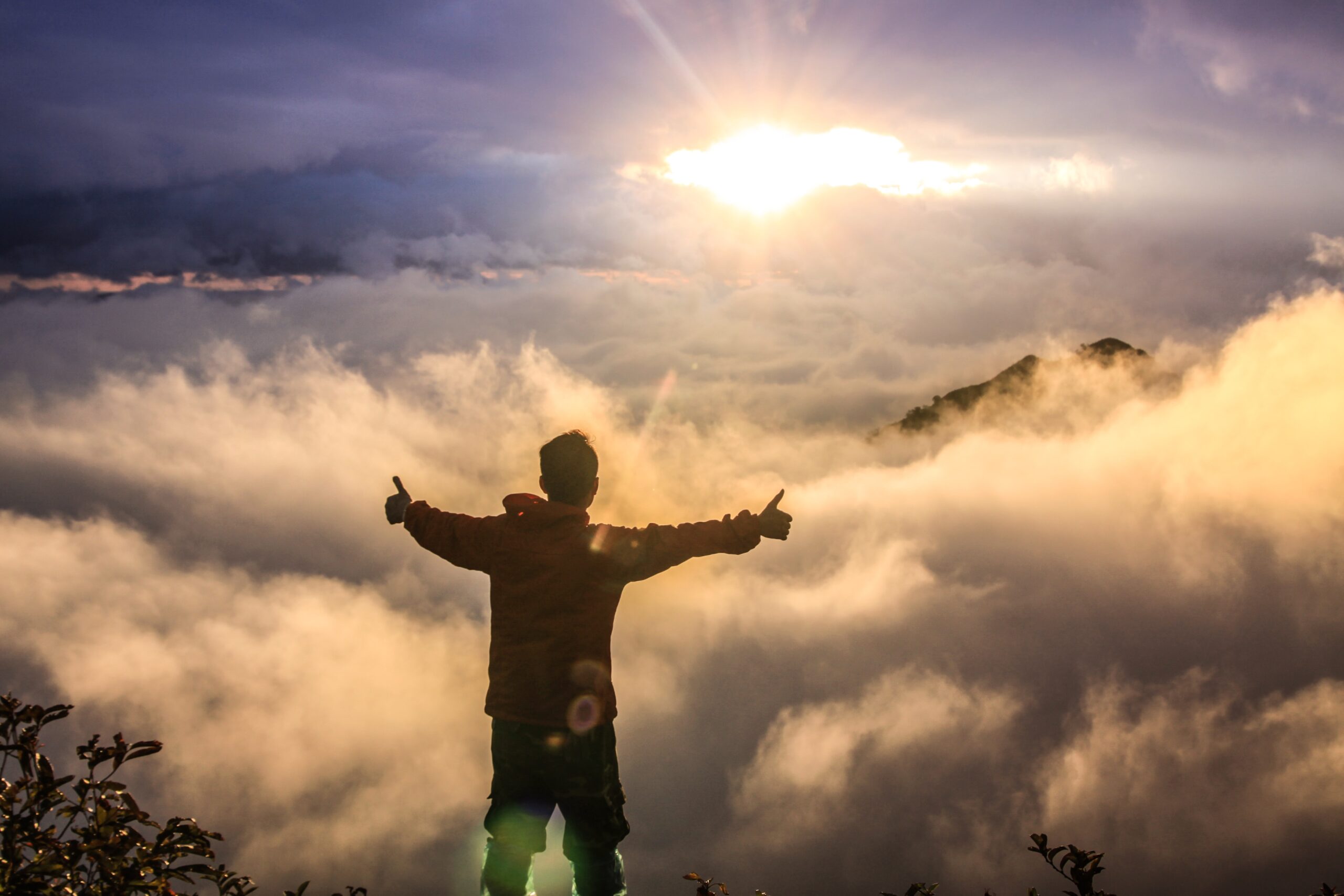 Silhouette of a man with outstretched arms as sunsets over fluffy clouds