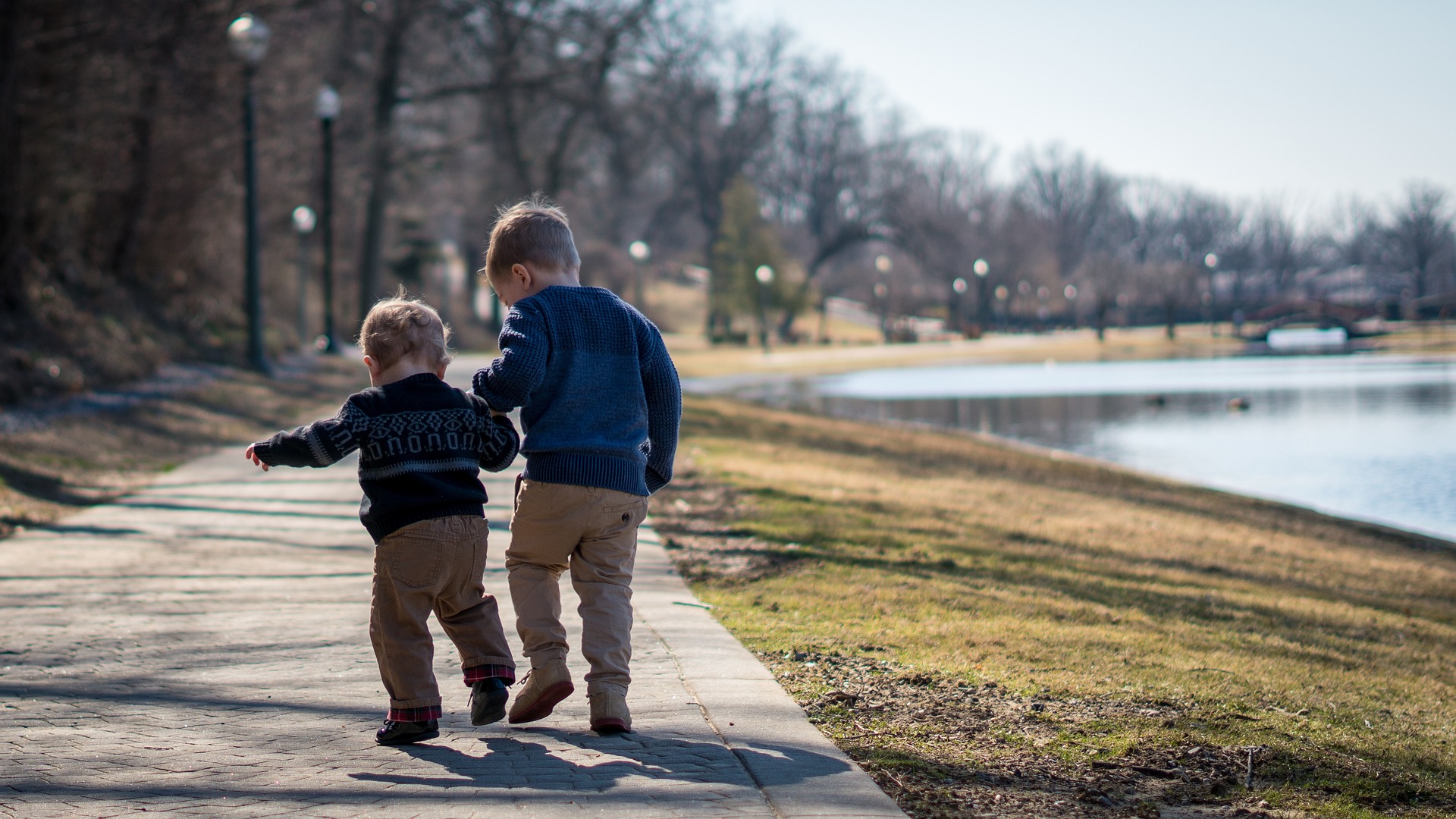 Toddlers helping each other walk around a lake