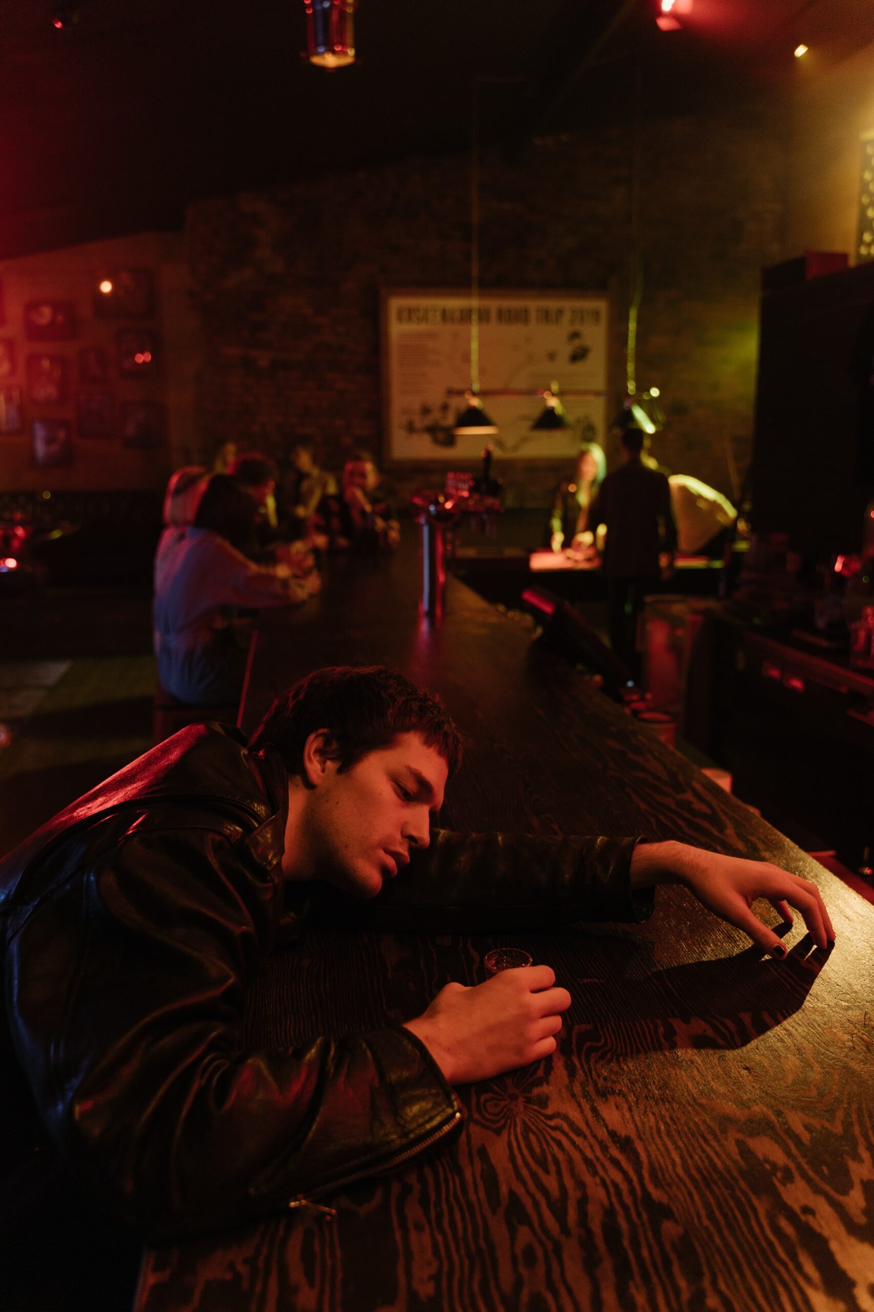 Drunk young man asleep on a bar with friends enjoying in the background