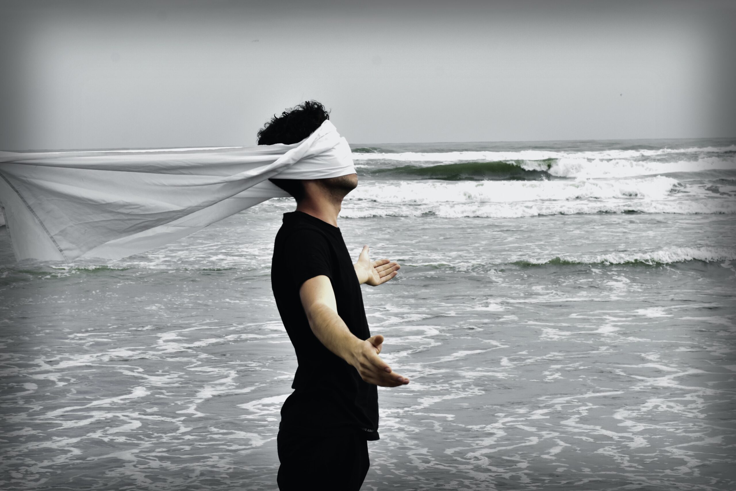 Man in black blind-folded in white cloth standing in the ocean