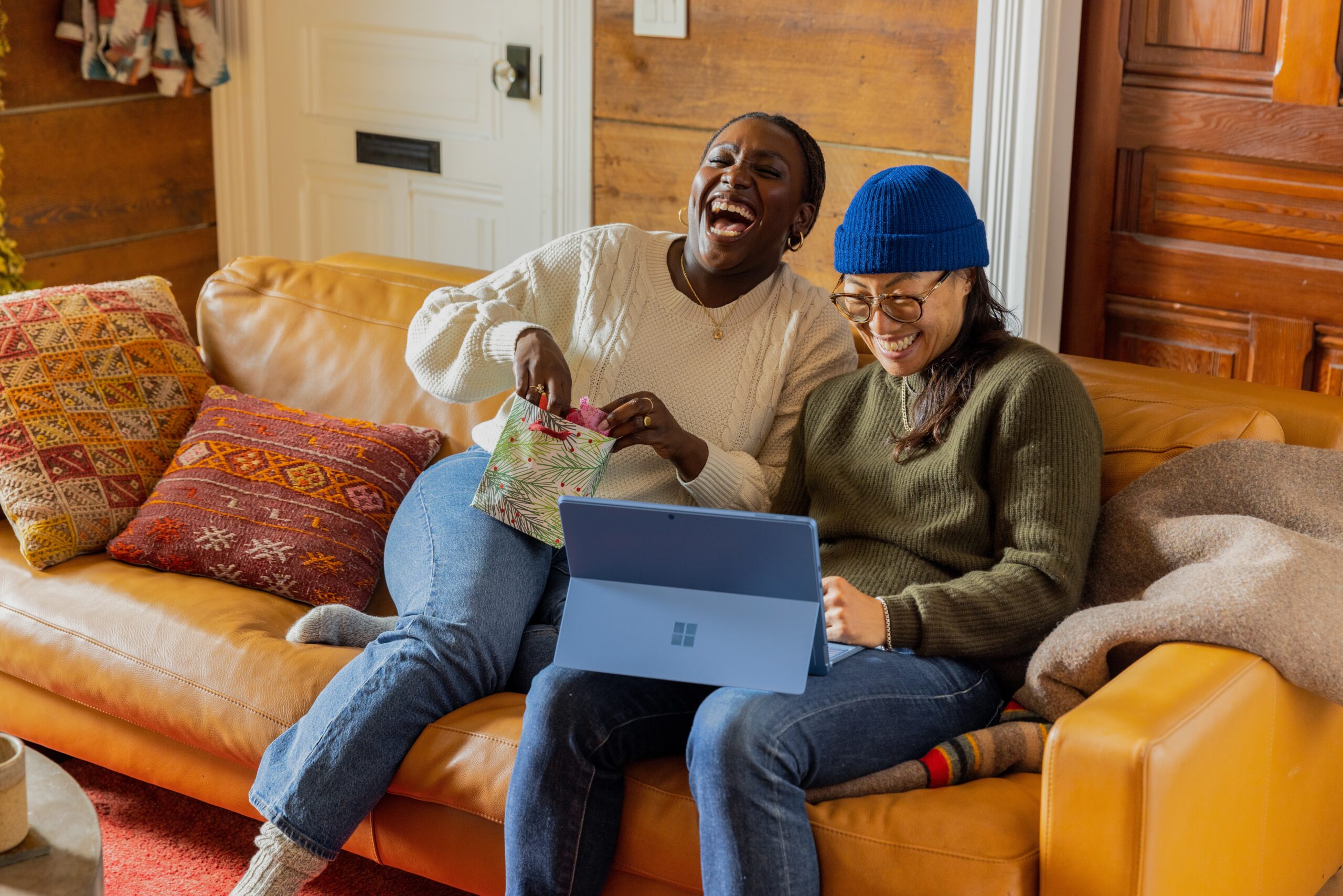 Two women laughing on a couch with a laptop