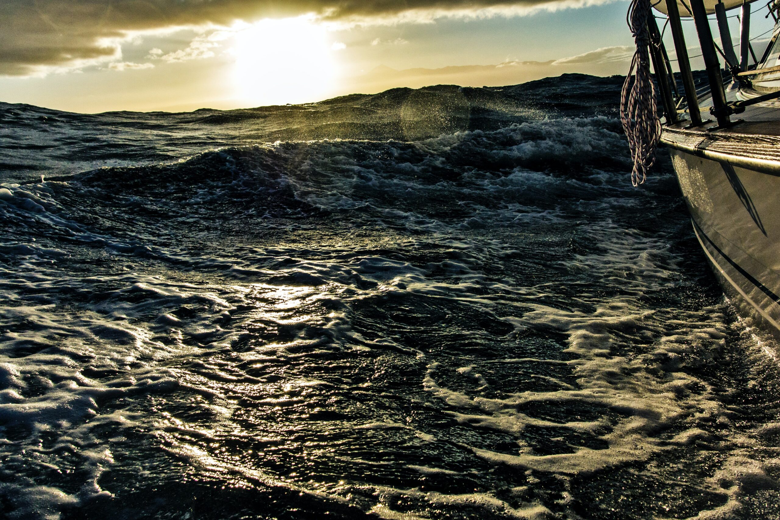 The bow of a ship heading through choppy waters to the sunset.