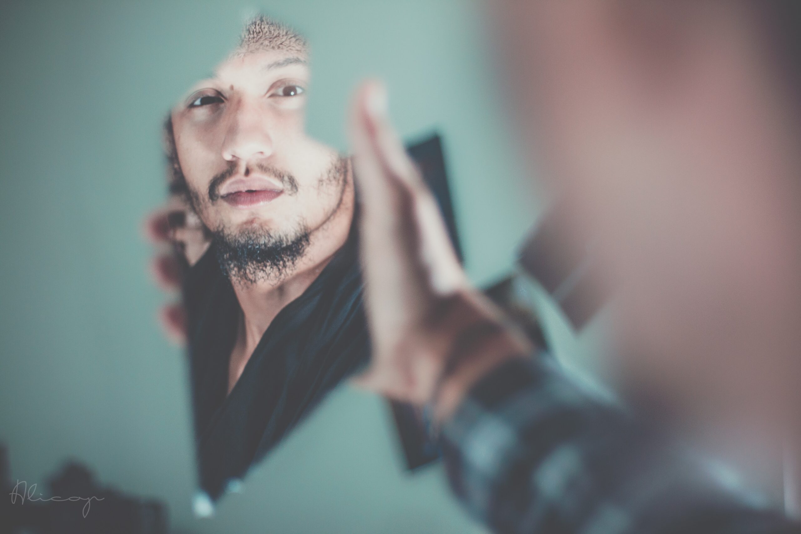 A bearded young man looking into a broken mirror