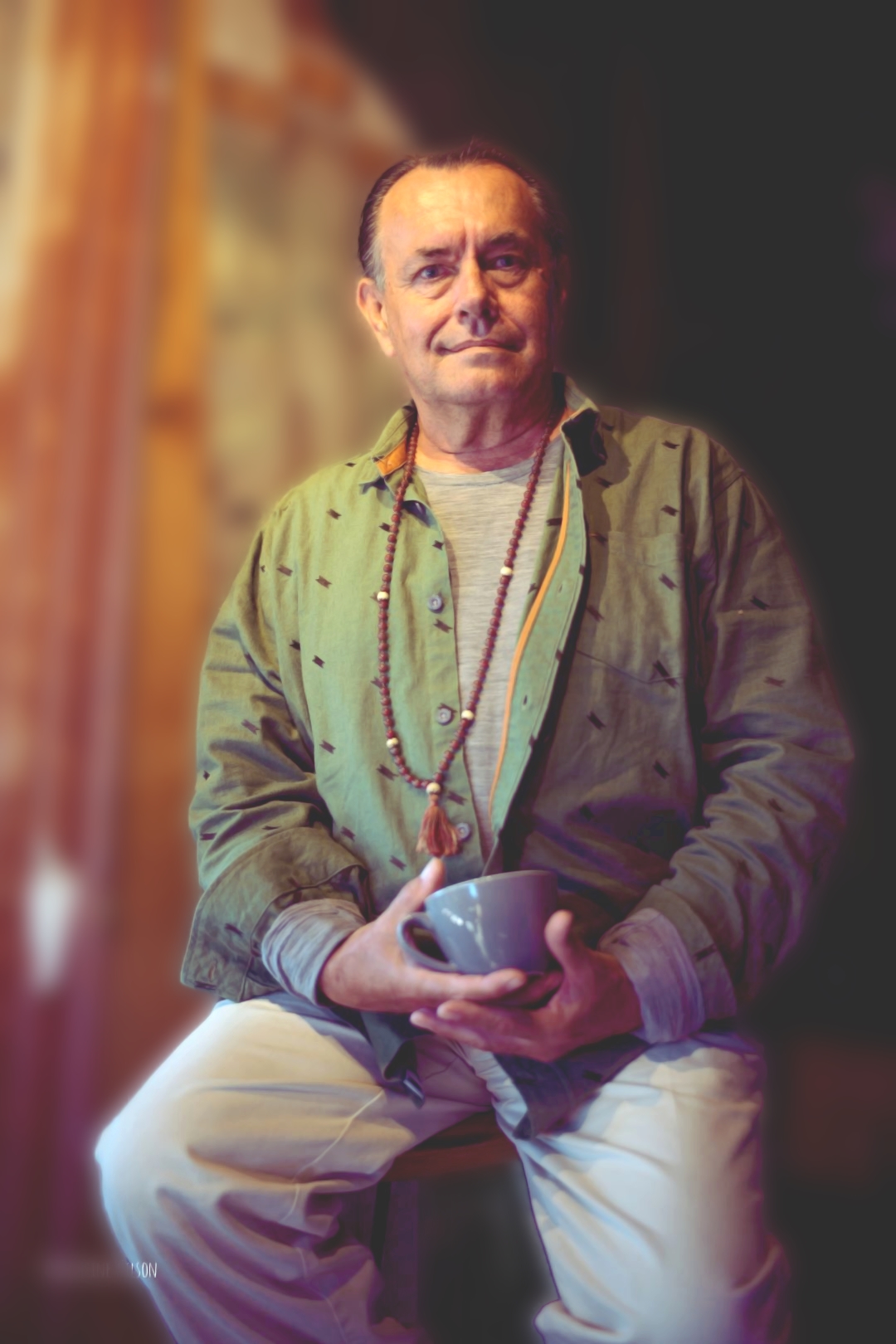 man in a green shirt wearing mala beads sitting on a bar stool