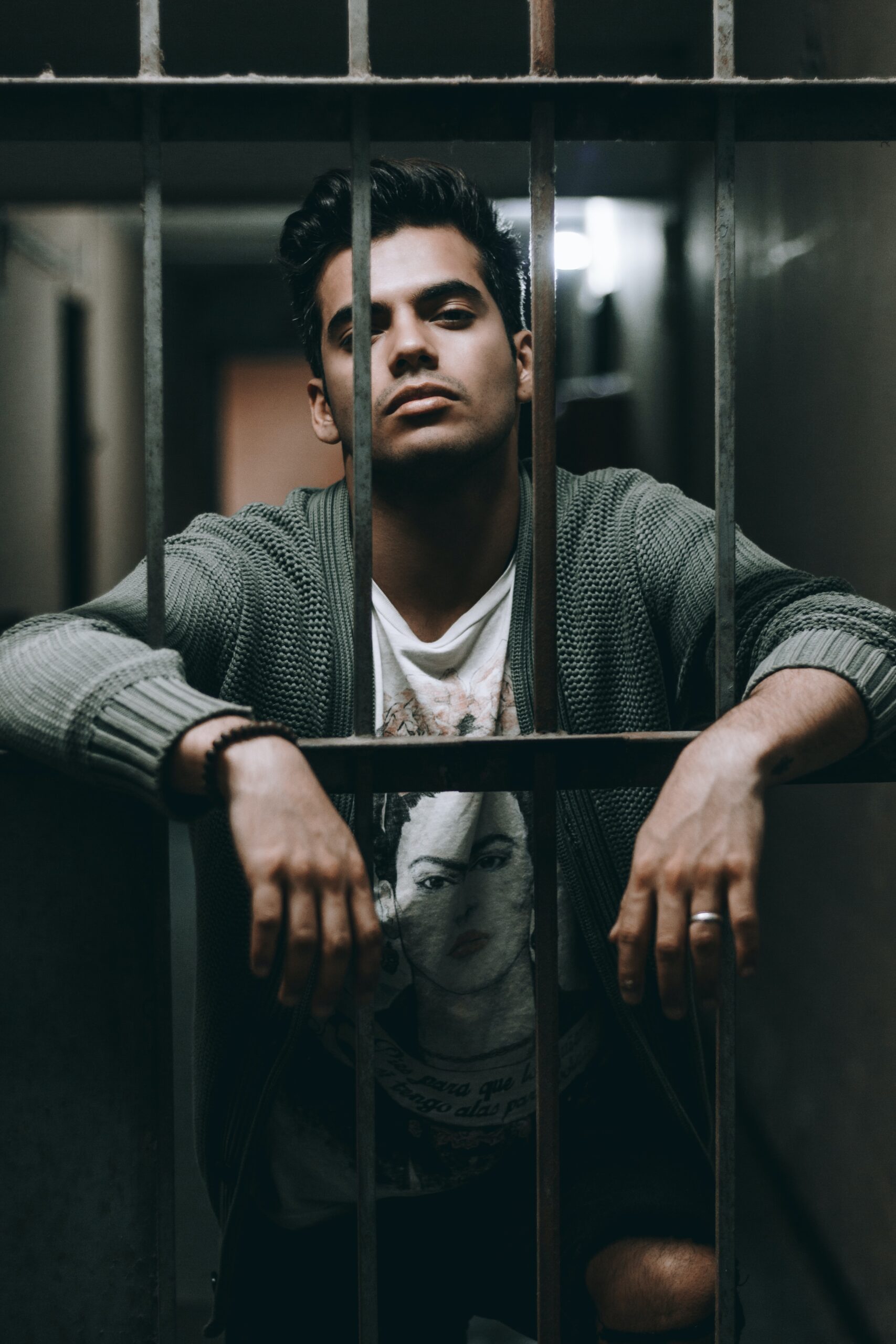 A young brown man behind bars in a green jumper