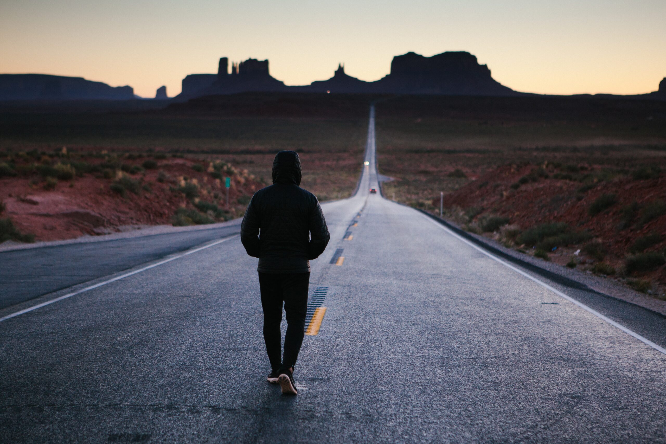Hooded person walking into the sunset along a deserted country road