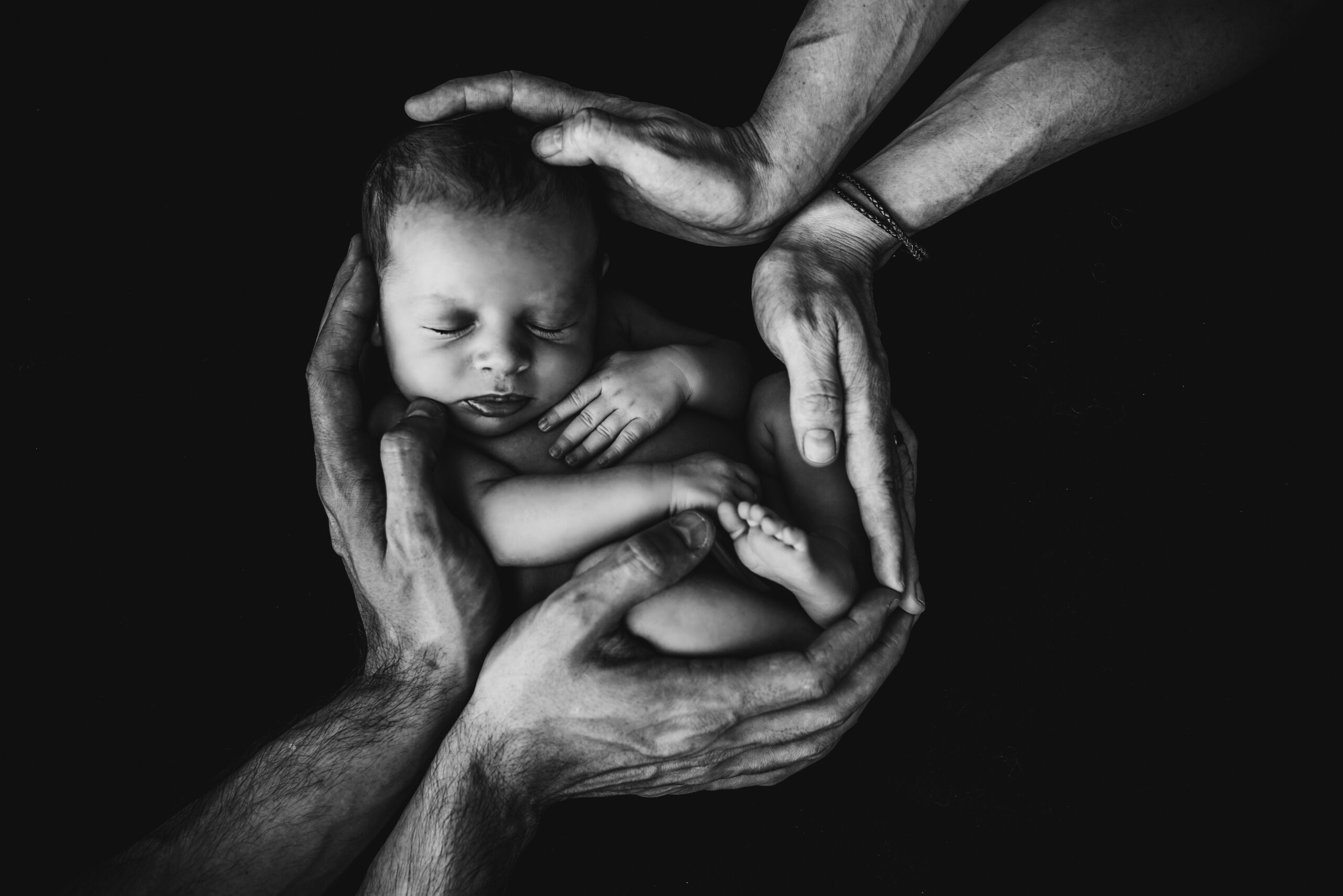 Black and white photo of parents hands holding a newborn baby