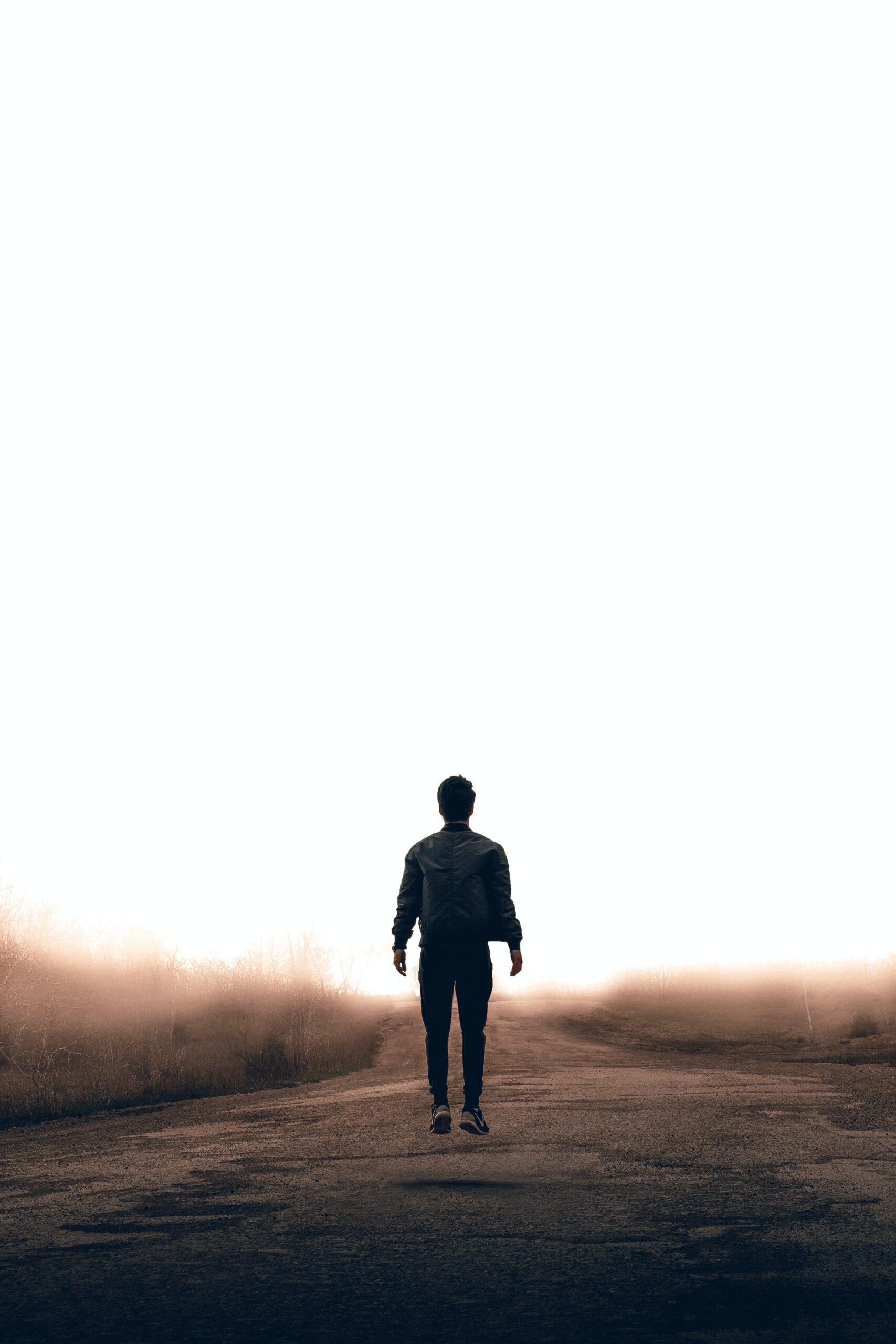 The silhouette of a man walking away along a country road