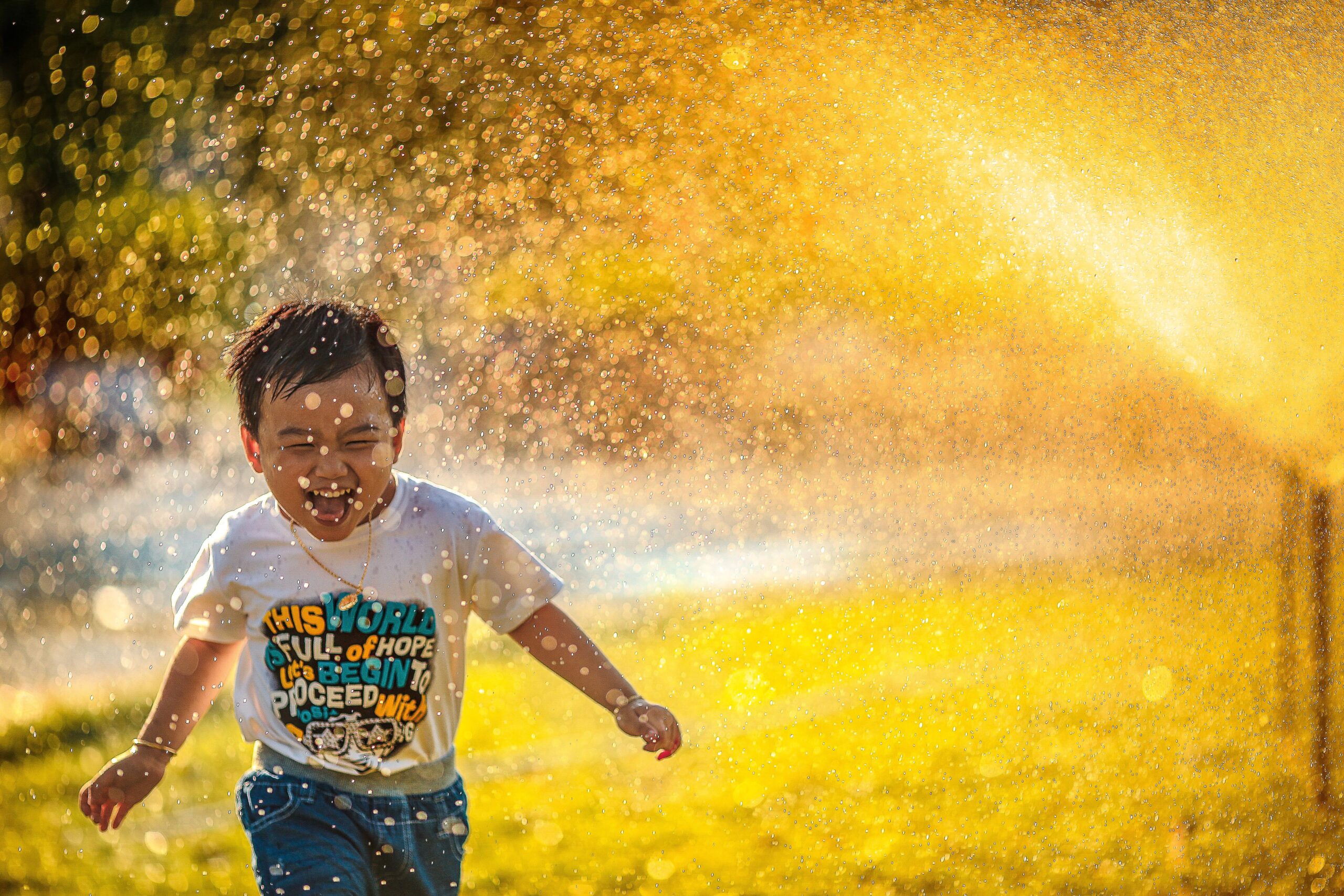 A toddler running through a sprinkler in golden sunshine