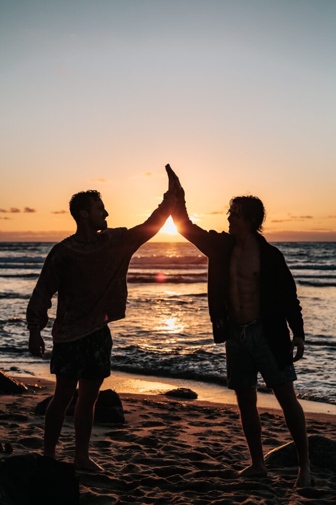 Silhouette of two men high fiving on a beach at sunset