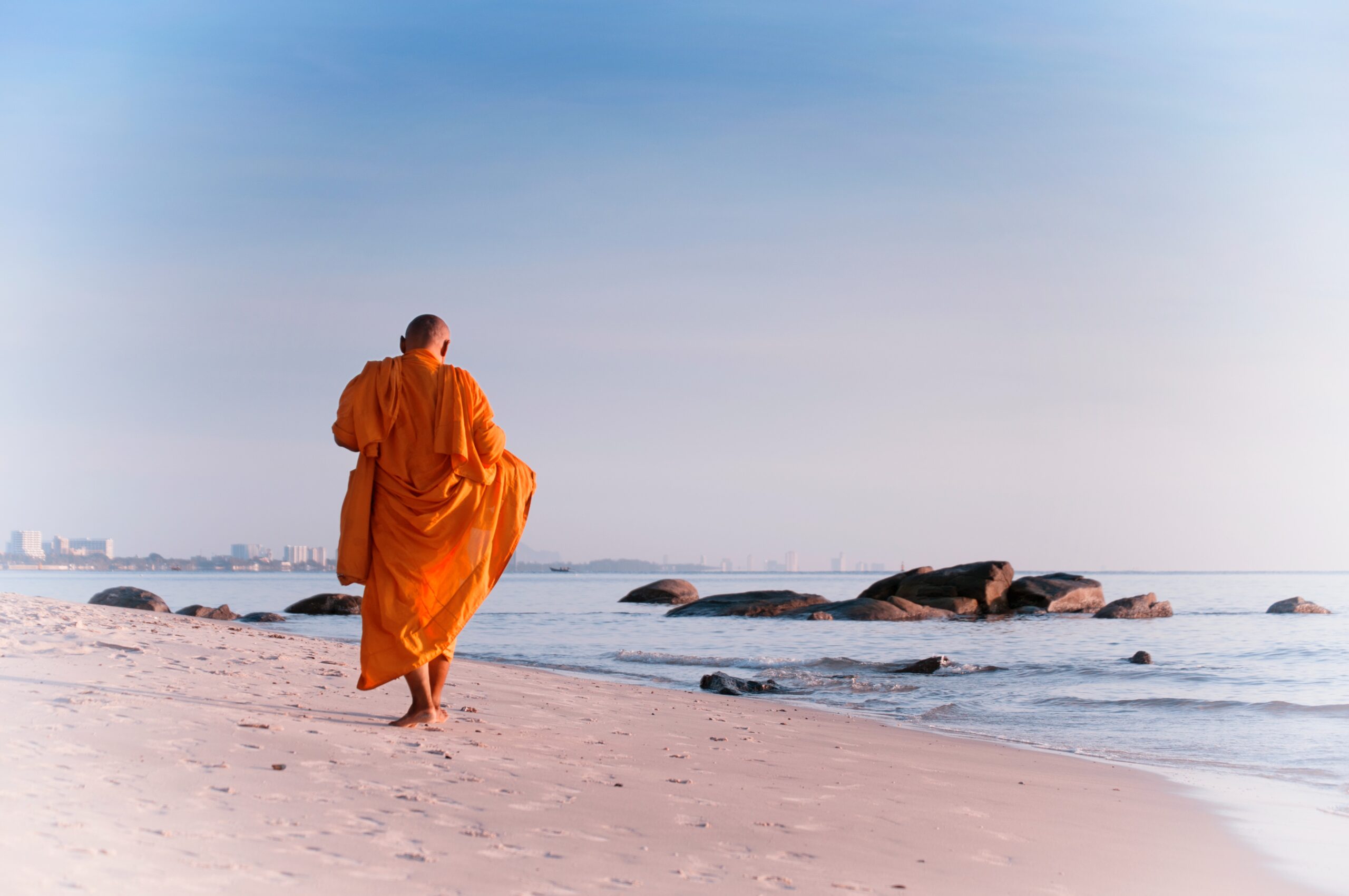 Orange robed monk walking on a secluded beach