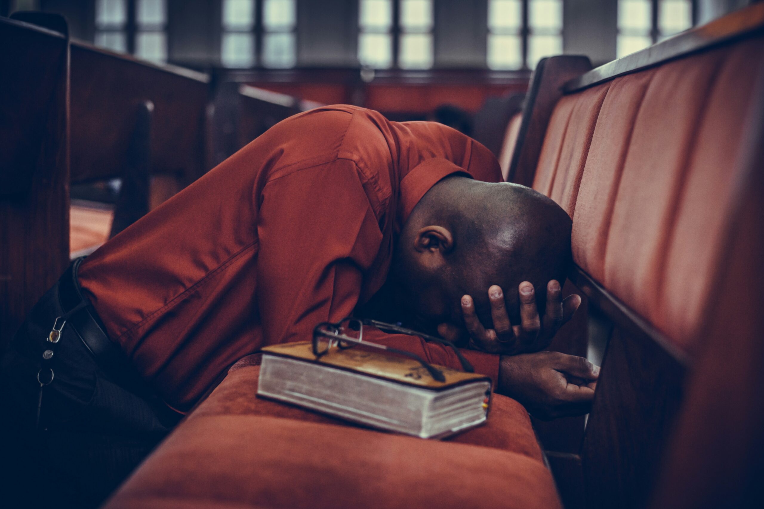 A man in a church crying, with a book beside him