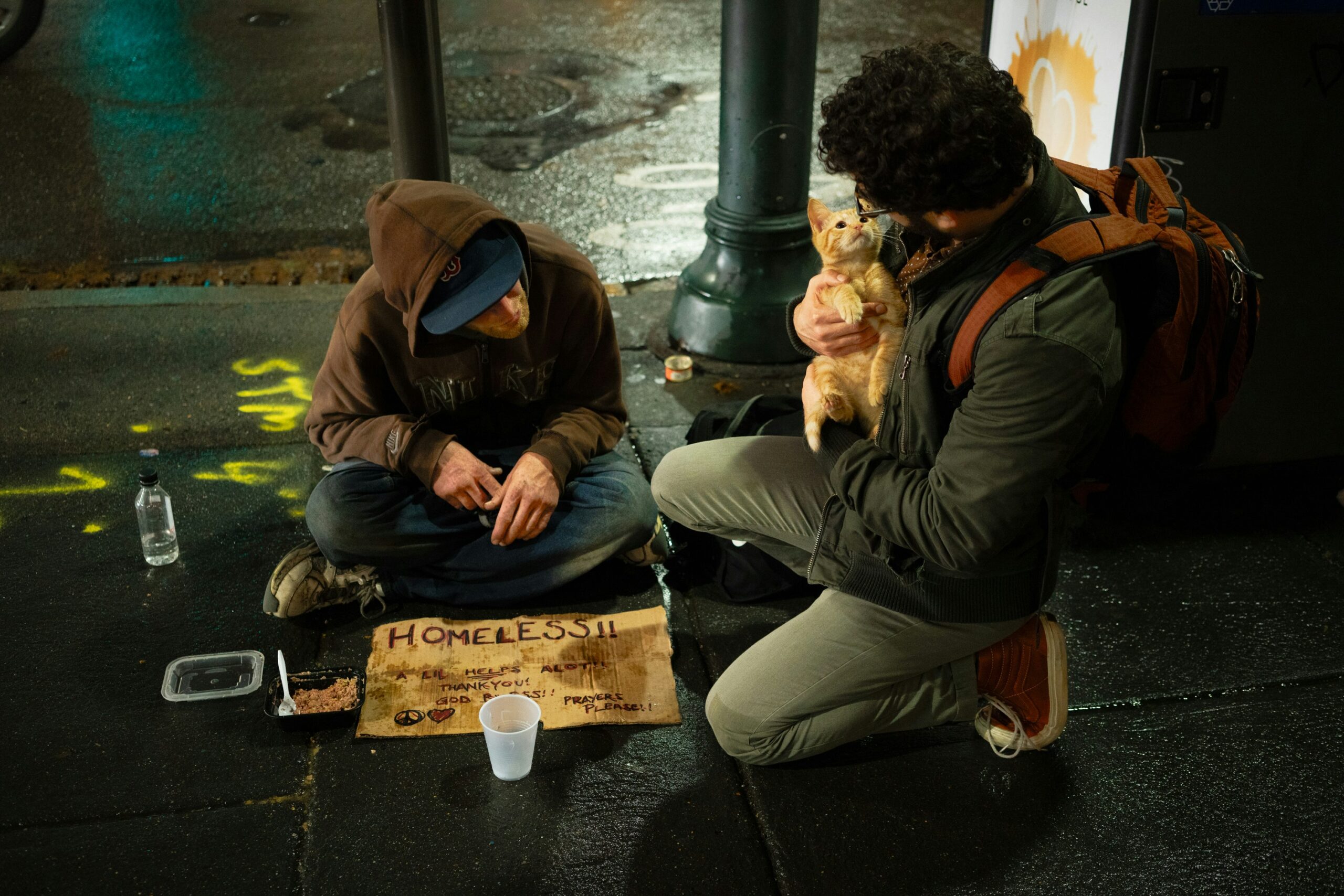 A person holding a cat is helping a beggar in the street