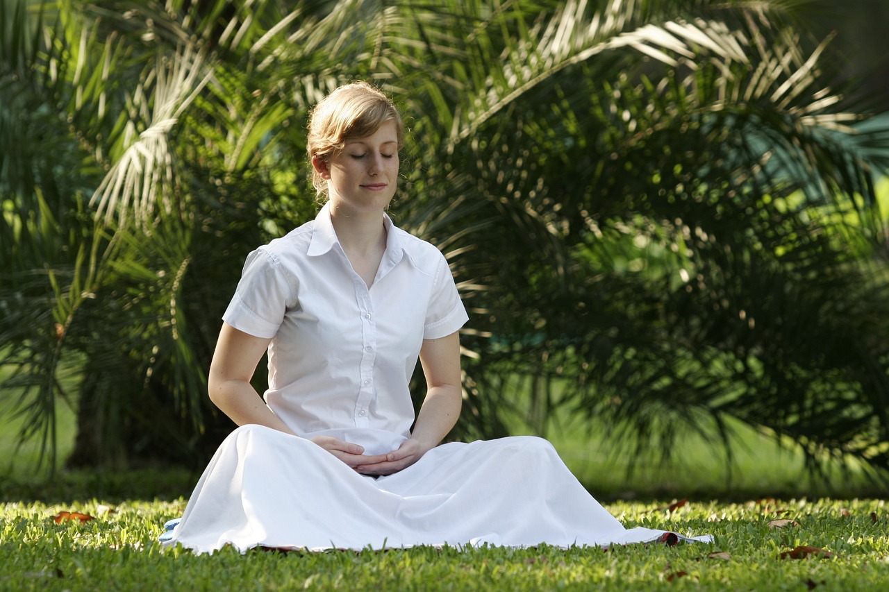 Woman in a white dress meditating on the grass